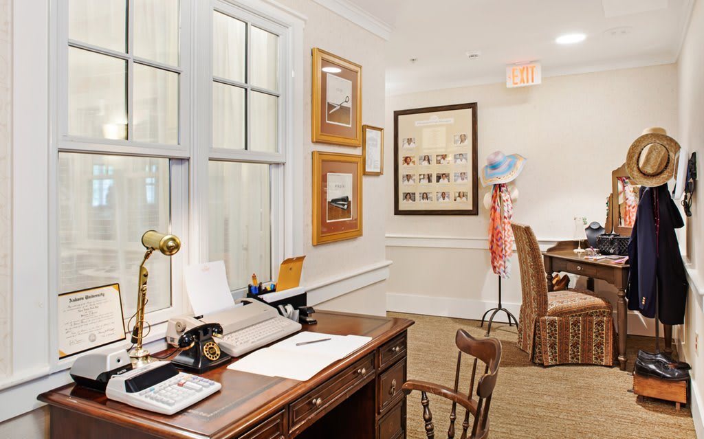 A vintage office space featuring a wooden desk with a typewriter and chair, decorated with framed pictures on the walls.