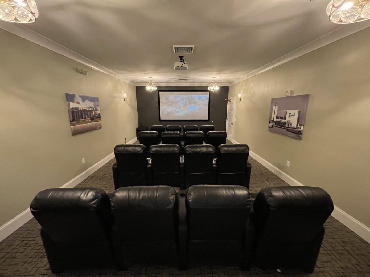 A cozy home theater setup with multiple rows of leather seating facing a large screen.