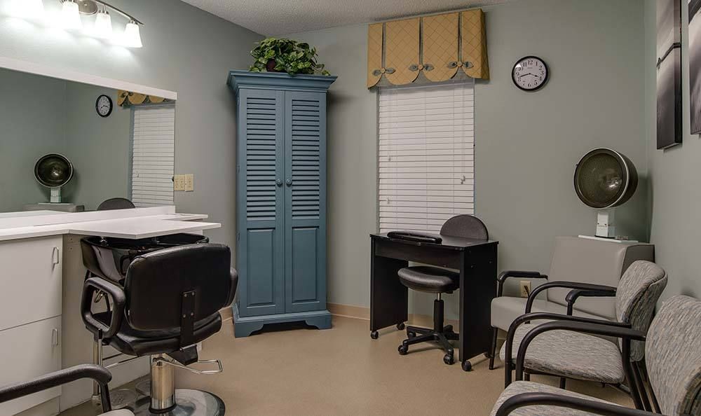 A cozy salon interior featuring chairs, a mirror, a blue cabinet, and a clock on the wall.