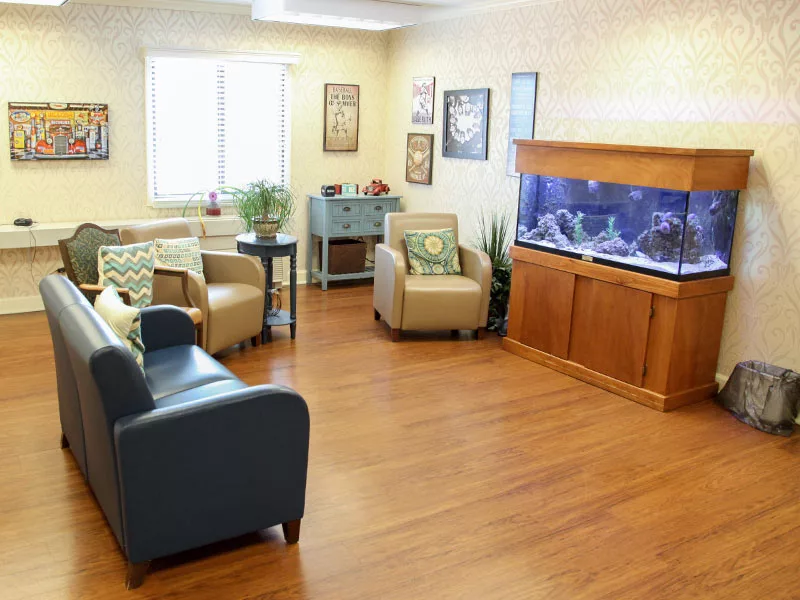 A cozy waiting room with comfortable chairs, an aquarium, and indoor plants.