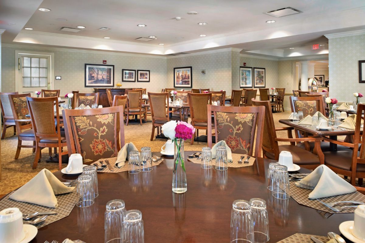 An elegant dining room setup with neatly arranged tables and chairs, decorated with flowers and glassware.