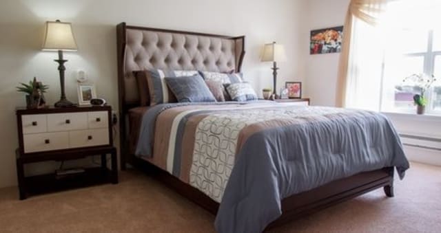 A cozy bedroom with a neatly made bed, featuring a tufted headboard and soft pillows.