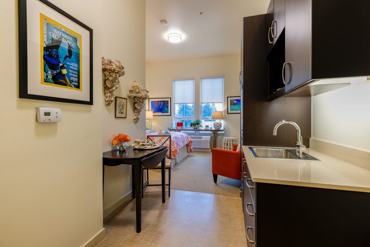 A cozy interior featuring a kitchenette leading to a brightly lit living area, adorned with artwork and stylish furniture.