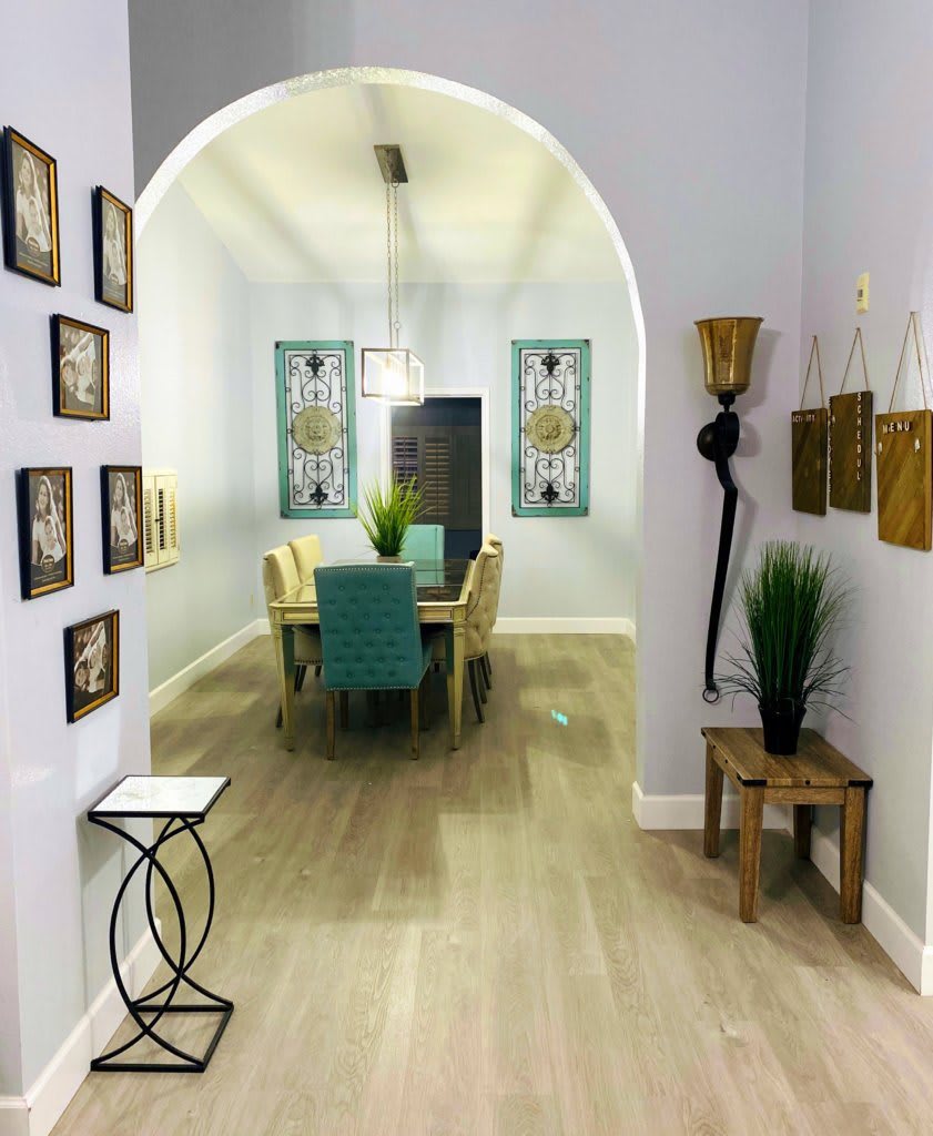 A modern dining room with stylish decor, featuring an archway, wooden flooring, and vibrant wall art.