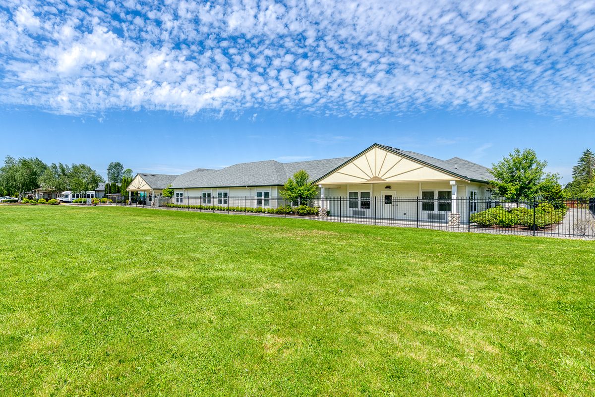 A single-story building with a large green lawn under a blue sky with clouds.