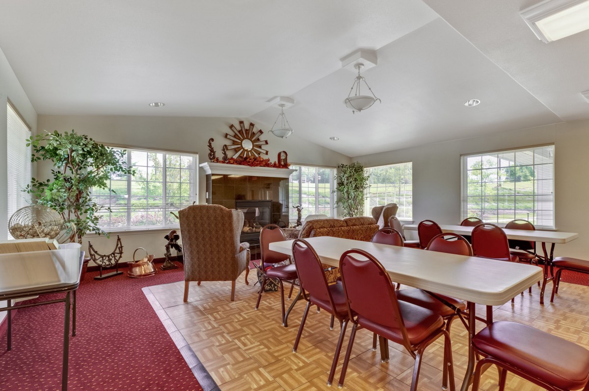 A spacious living room with red chairs and tables, featuring large windows and decorative elements on the walls.