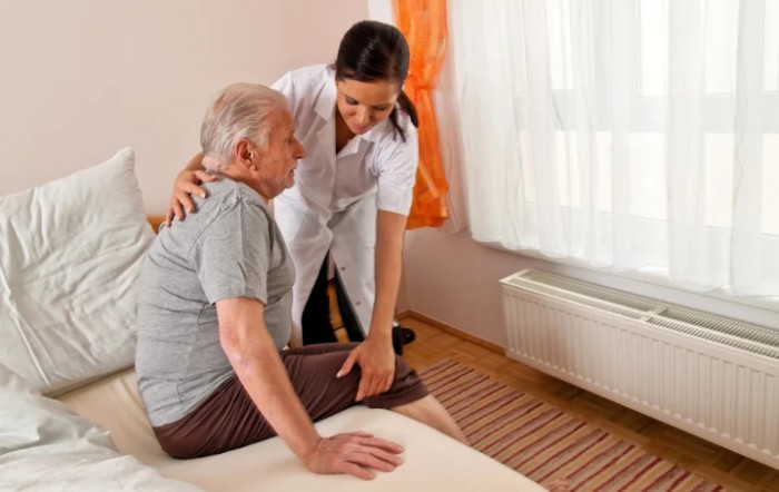 A nurse assists an elderly man in a care facility.