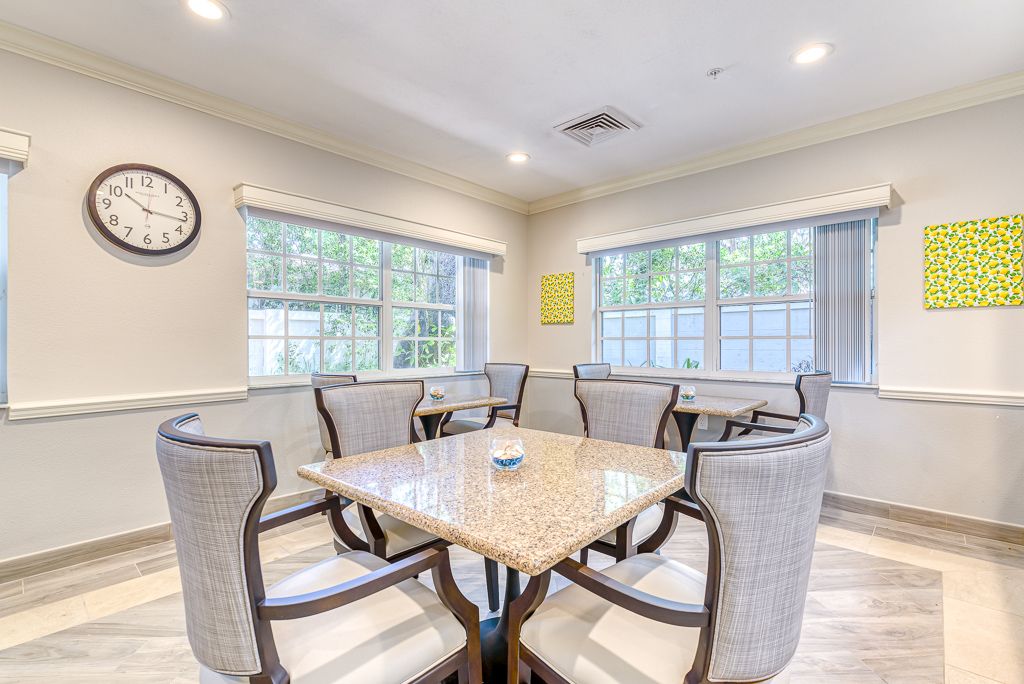 A bright and modern dining room with a square table and upholstered chairs, surrounded by large windows.