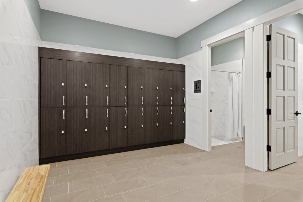 A clean and organized locker room featuring a row of dark lockers and a shower area.