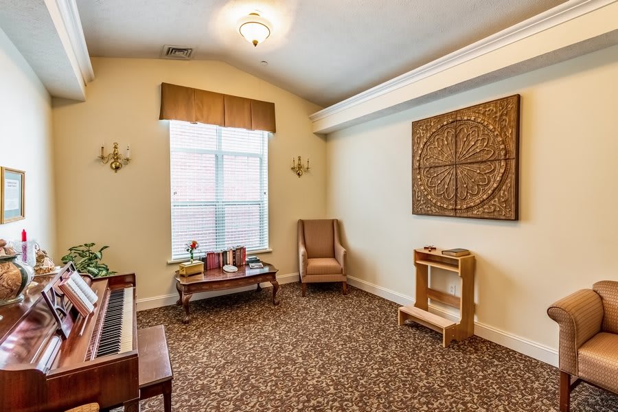 A cozy room featuring a piano, window, and comfortable seating with decorative artwork on the wall.