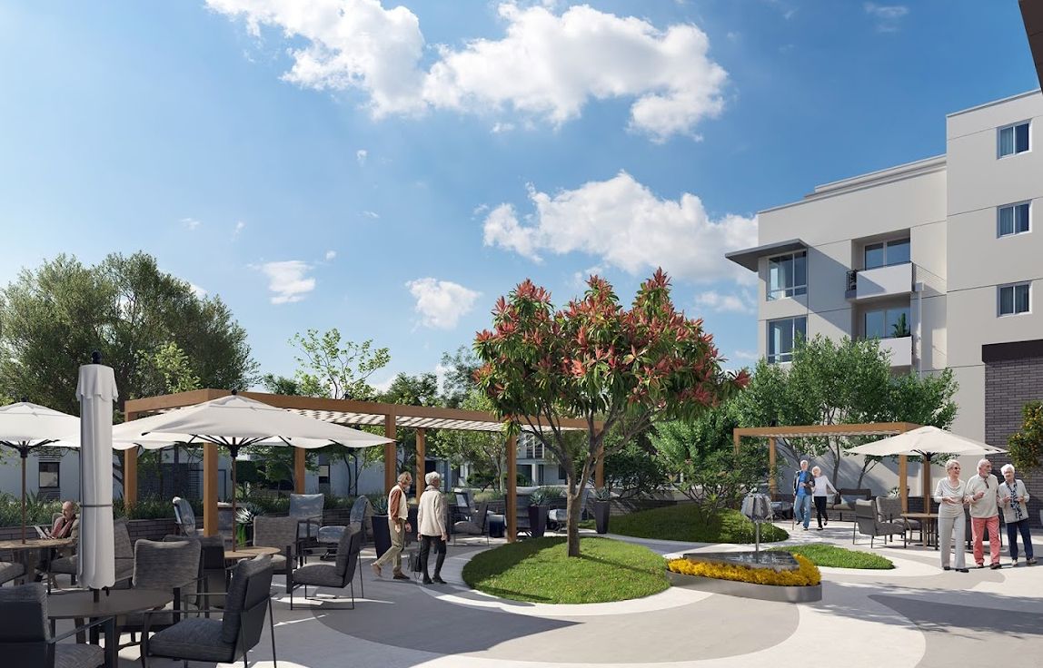 A lively outdoor patio scene with people enjoying the sunshine among trees and garden furniture.
