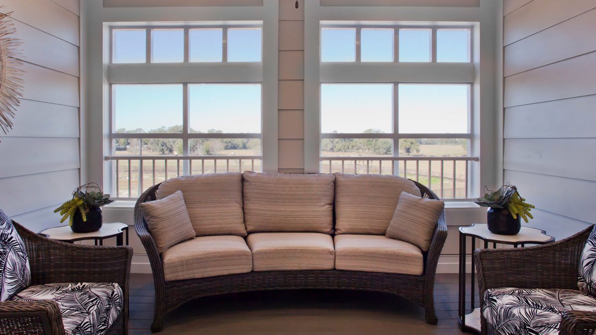 A wicker sofa with cushions positioned in front of large windows, allowing natural light to fill the room.