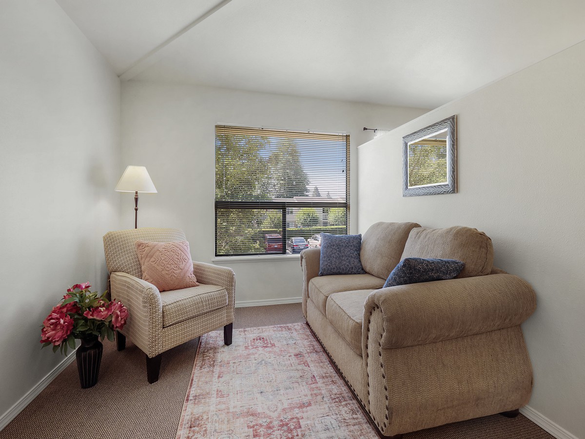 A cozy living room with a sofa, armchair, and a window overlooking the outdoors.