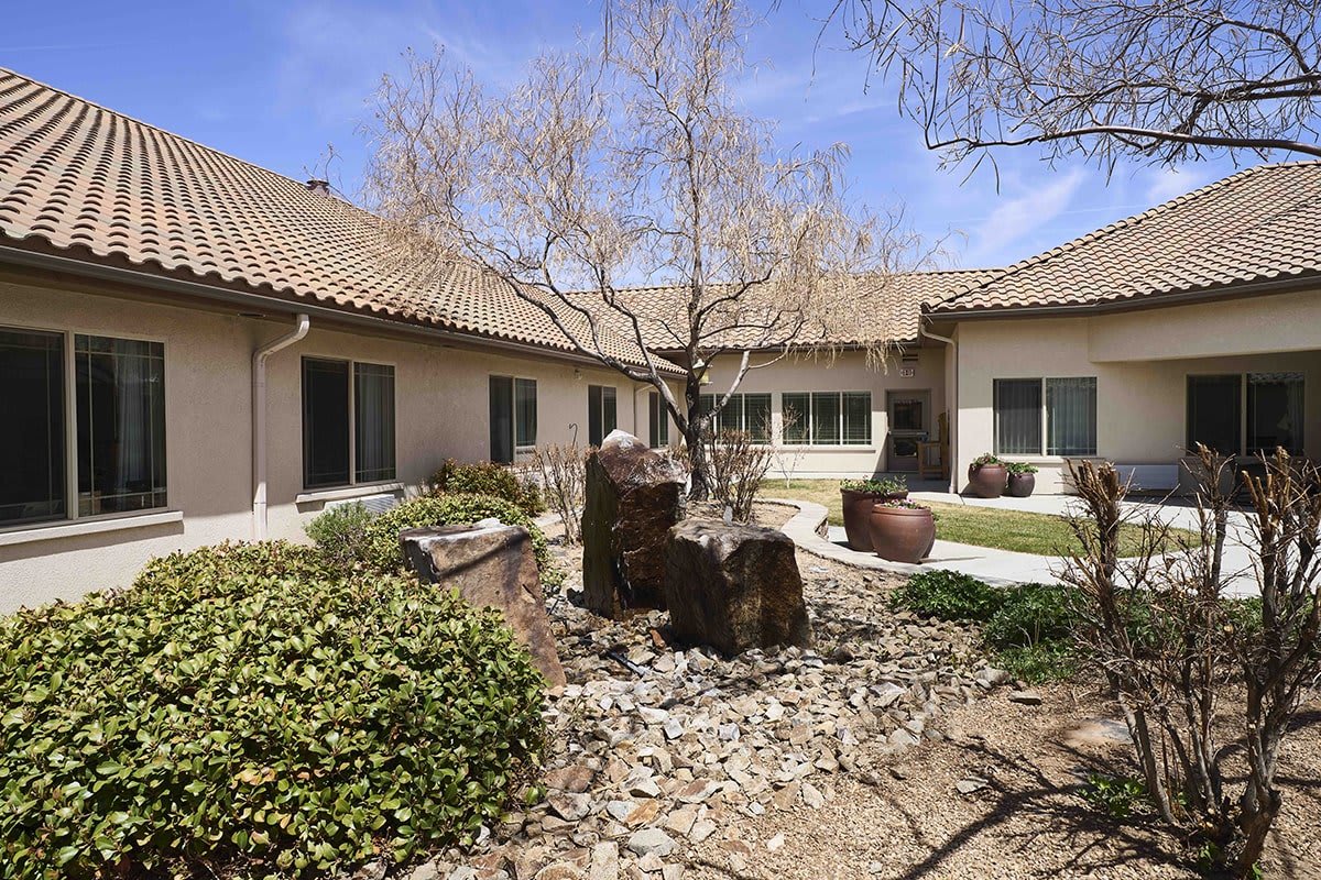 A serene courtyard with a tree and stone landscaping in front of a house.