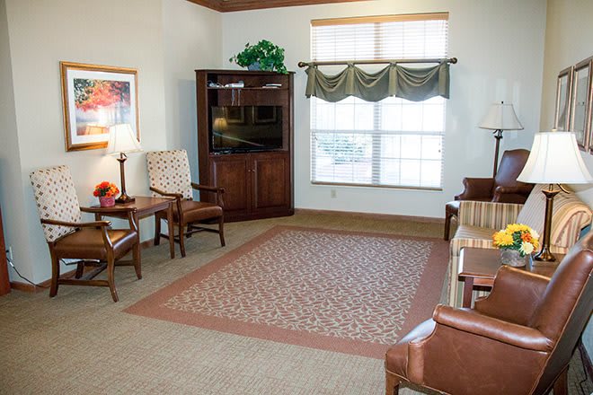 A cozy living room with a television, chairs, and a large window.