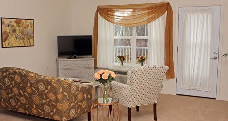 Cozy living room with patterned chairs, a TV, and elegant window drapes.