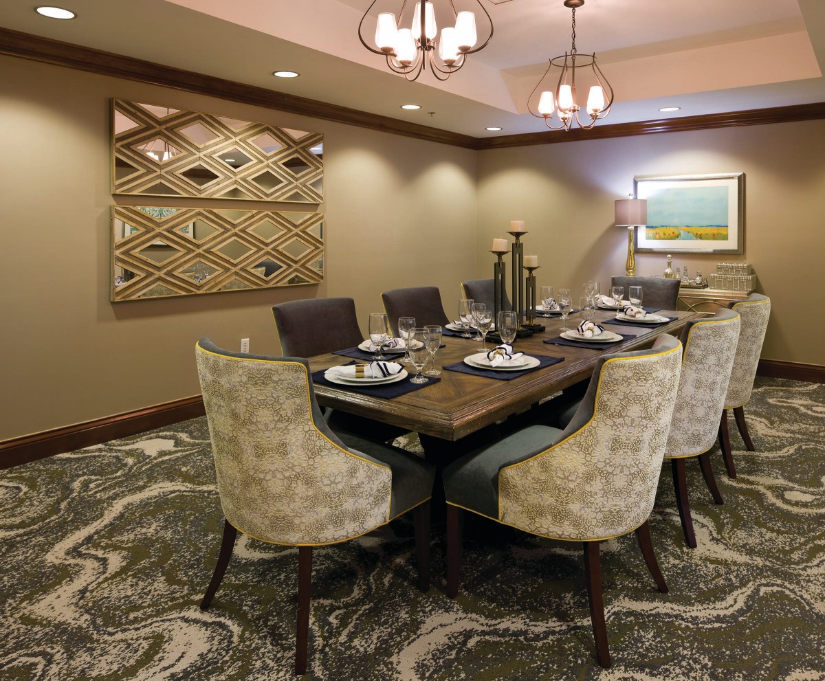 A well-decorated dining room with a large table, chairs, artwork on the wall, and elegant lighting.