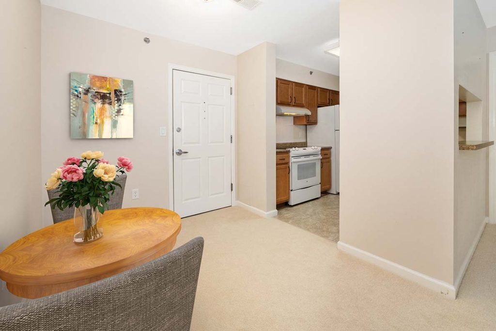 A cozy apartment interior featuring a small kitchen and dining area with a round table, chairs, and flowers on the table.