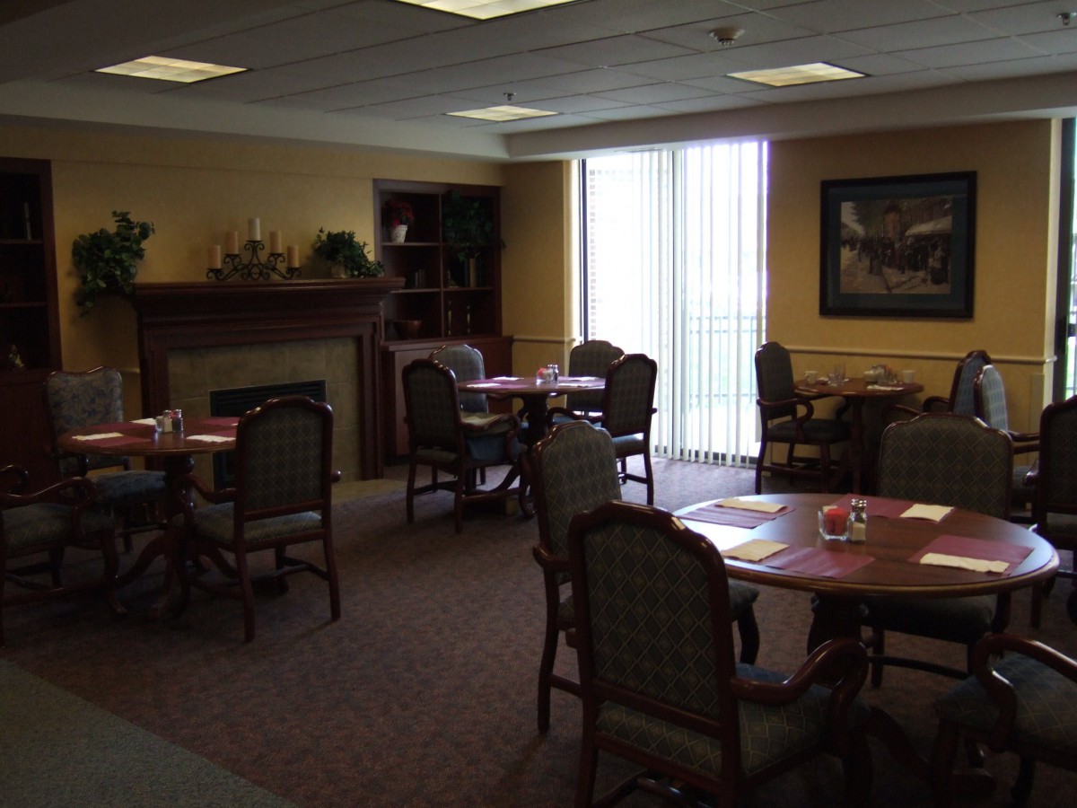 A cozy dining room with several tables and chairs, a fireplace, and large windows.
