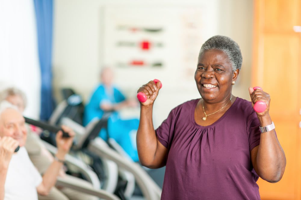 A senior woman smiling while exercising with dumbbells in a gym.