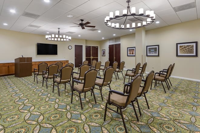 An empty conference room with arranged chairs, chandeliers, and a television.