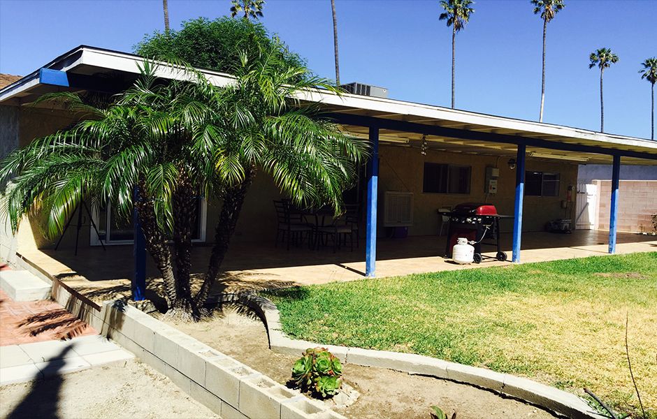 A house with a covered porch and palm trees on a sunny day.