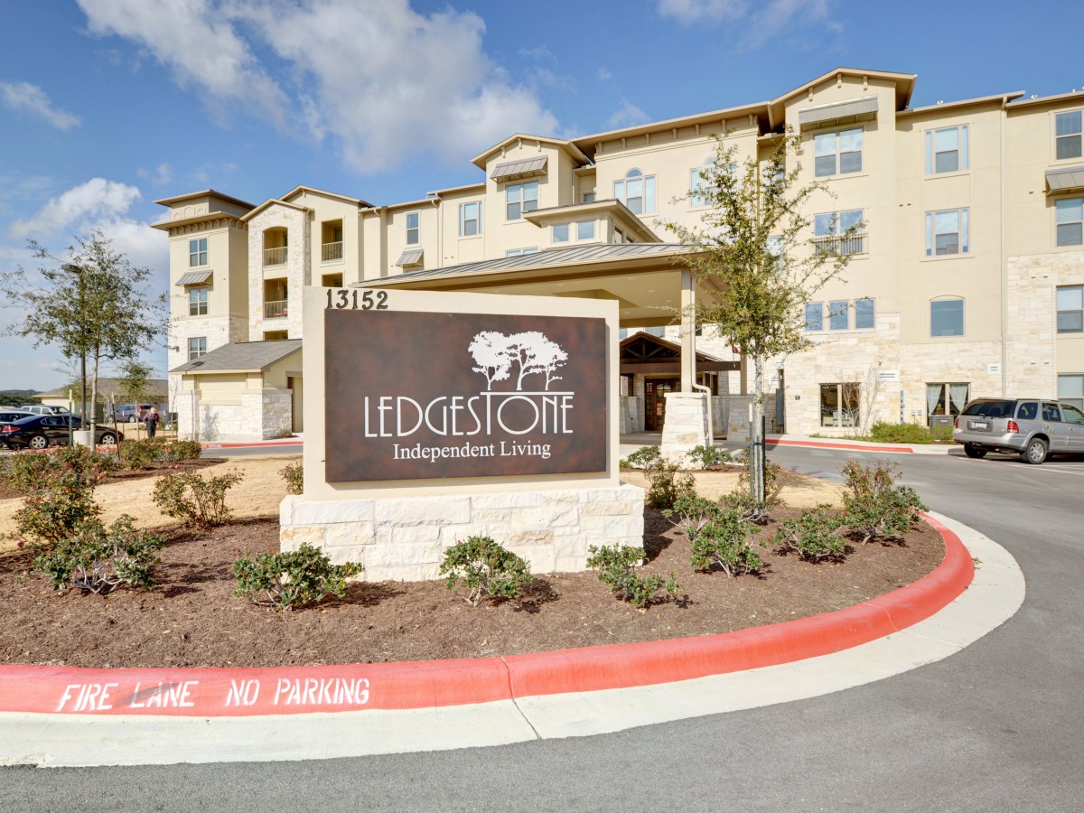 The image shows the exterior of a residential apartment complex with a prominent sign that reads 'Ledgestone Independent Living'.