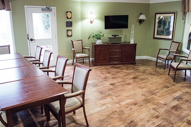 A well-lit conference room with chairs arranged along a table, featuring a television and wooden flooring.