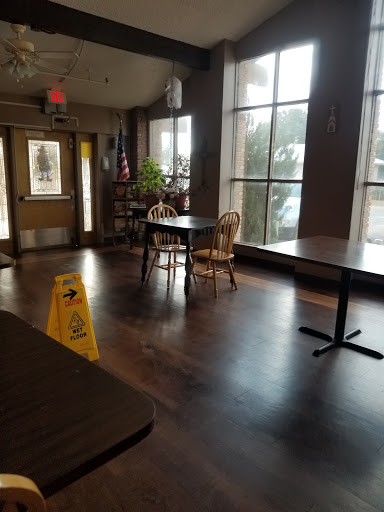 A quiet and empty restaurant interior featuring tables and chairs, with a caution sign on the floor.