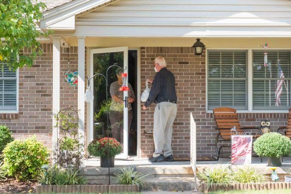 A visitor stands at the front door of a brick house, engaging with someone inside.