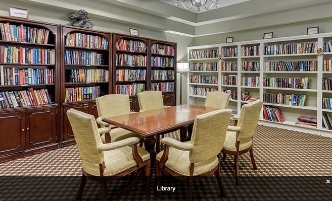 A cozy library with bookshelves and a reading table surrounded by chairs.