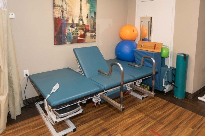 A physical therapy room equipped with an adjustable table and exercise balls.
