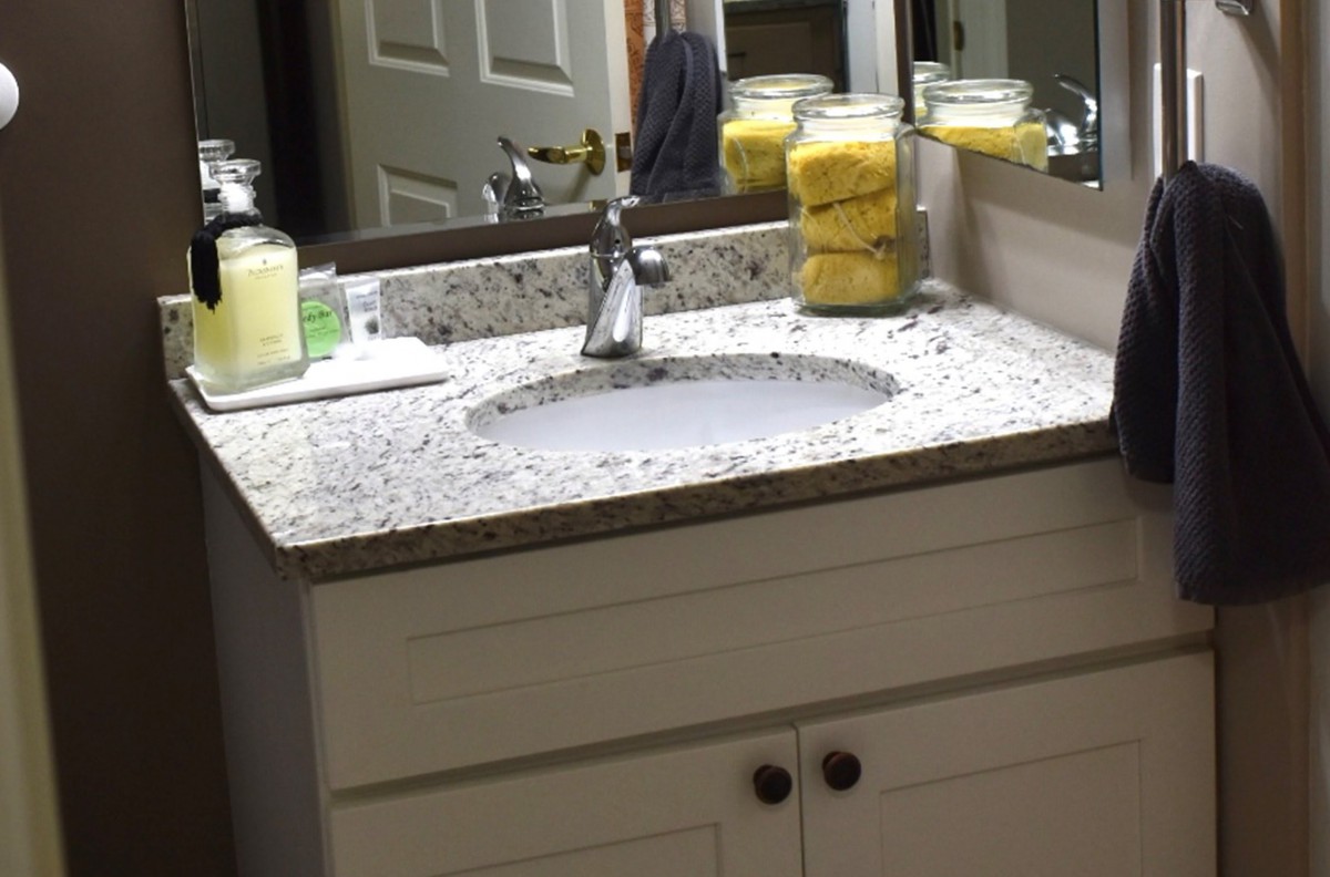 A clean bathroom sink with a granite countertop, featuring a soap dispenser and sponges in jars.