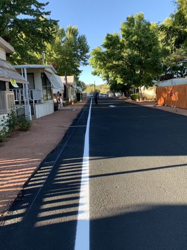 A quiet residential street lined with trees and houses, freshly paved with a white line down the center.