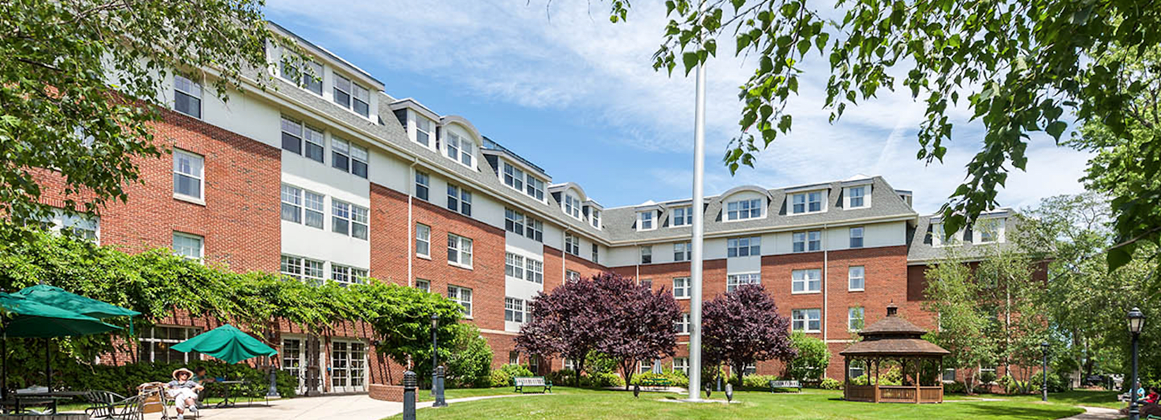 A multi-story brick residential building with a flagpole and trees in front.