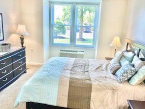 A cozy bedroom with a neatly made bed, side lamps, and a large window letting in natural light.