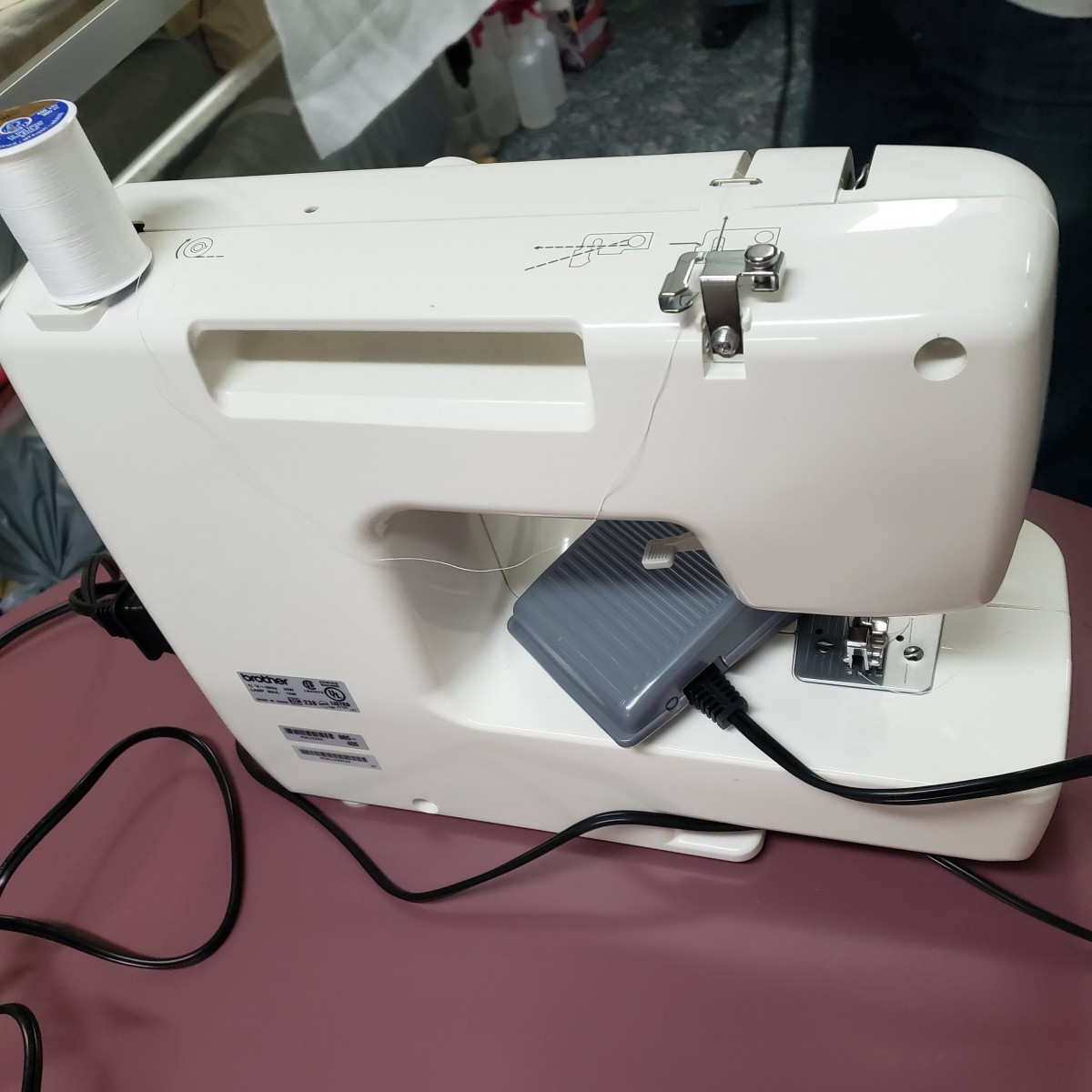A white electric sewing machine with a spool of blue thread is set up on a table.