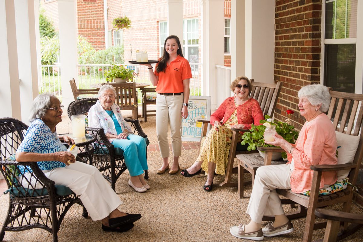 A group of elderly women socializing on a porch with a caretaker.