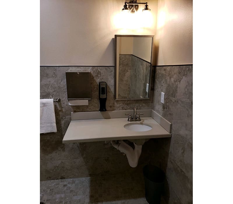 A bathroom with a sink, mirror, tile walls, and a mounted soap dispenser.