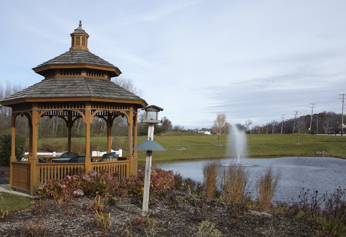 A peaceful gazebo stands beside a pond with a fountain in a serene landscape.