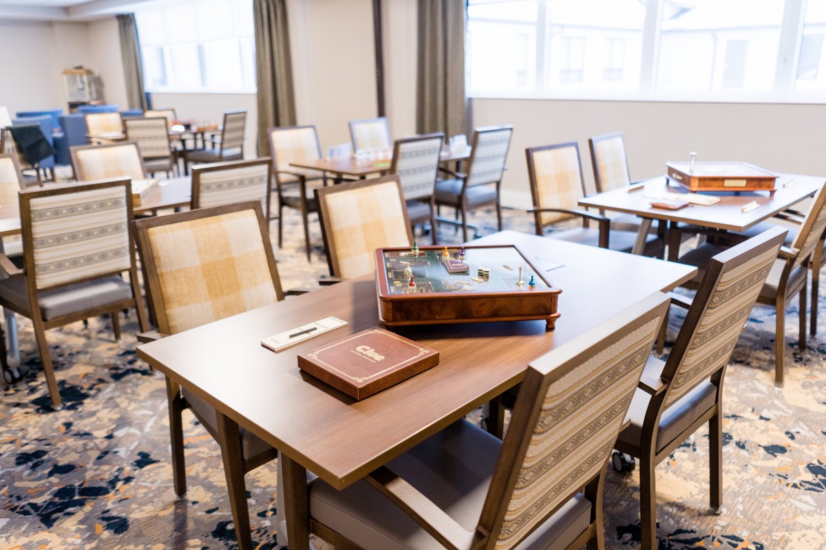 A neatly arranged dining room with wooden tables and chairs, featuring elegant place settings.