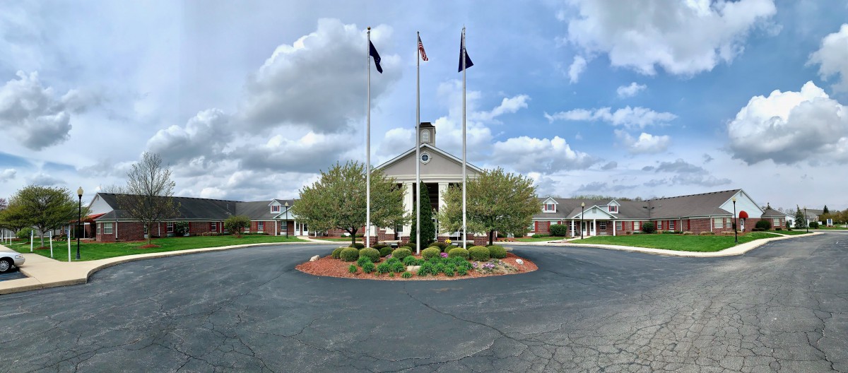 A large building with a central entrance, surrounded by a circular driveway and landscaped area, featuring three flags.