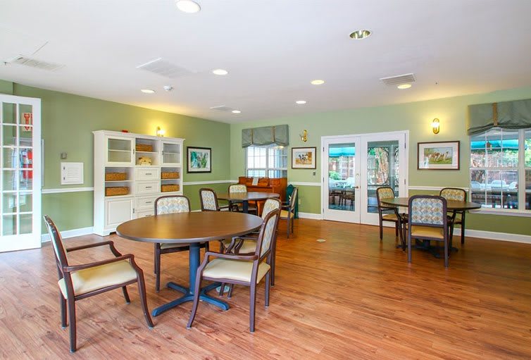 A cozy community room with seating arrangements, tables, and a shelving unit.