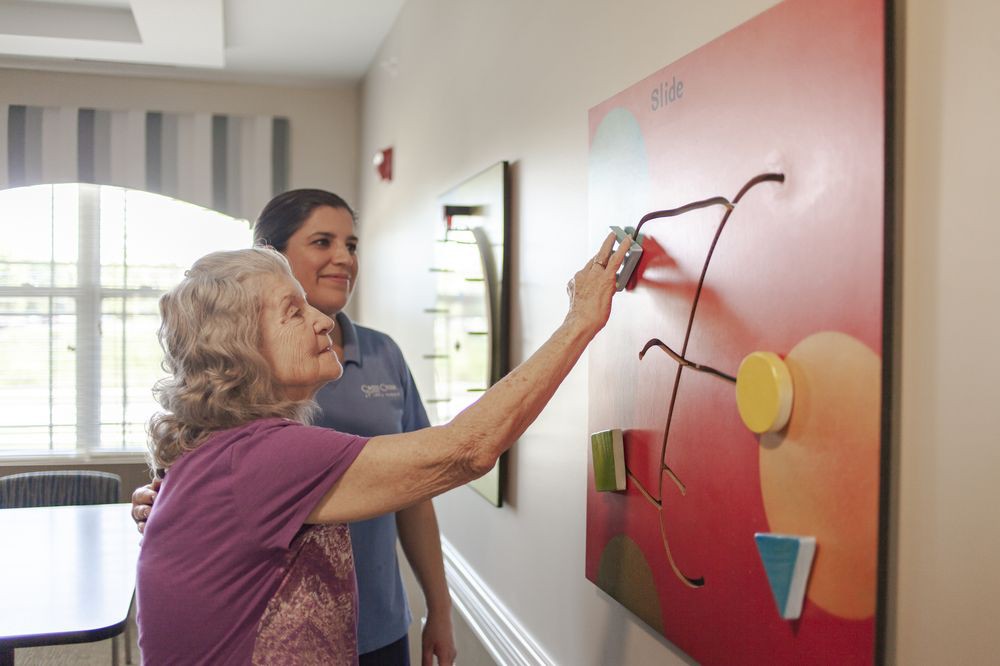 A senior woman engages in an activity with assistance from a caregiver.