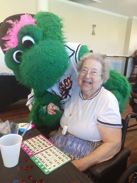 A cheerful elderly woman enjoys a bingo game with a friendly mascot.