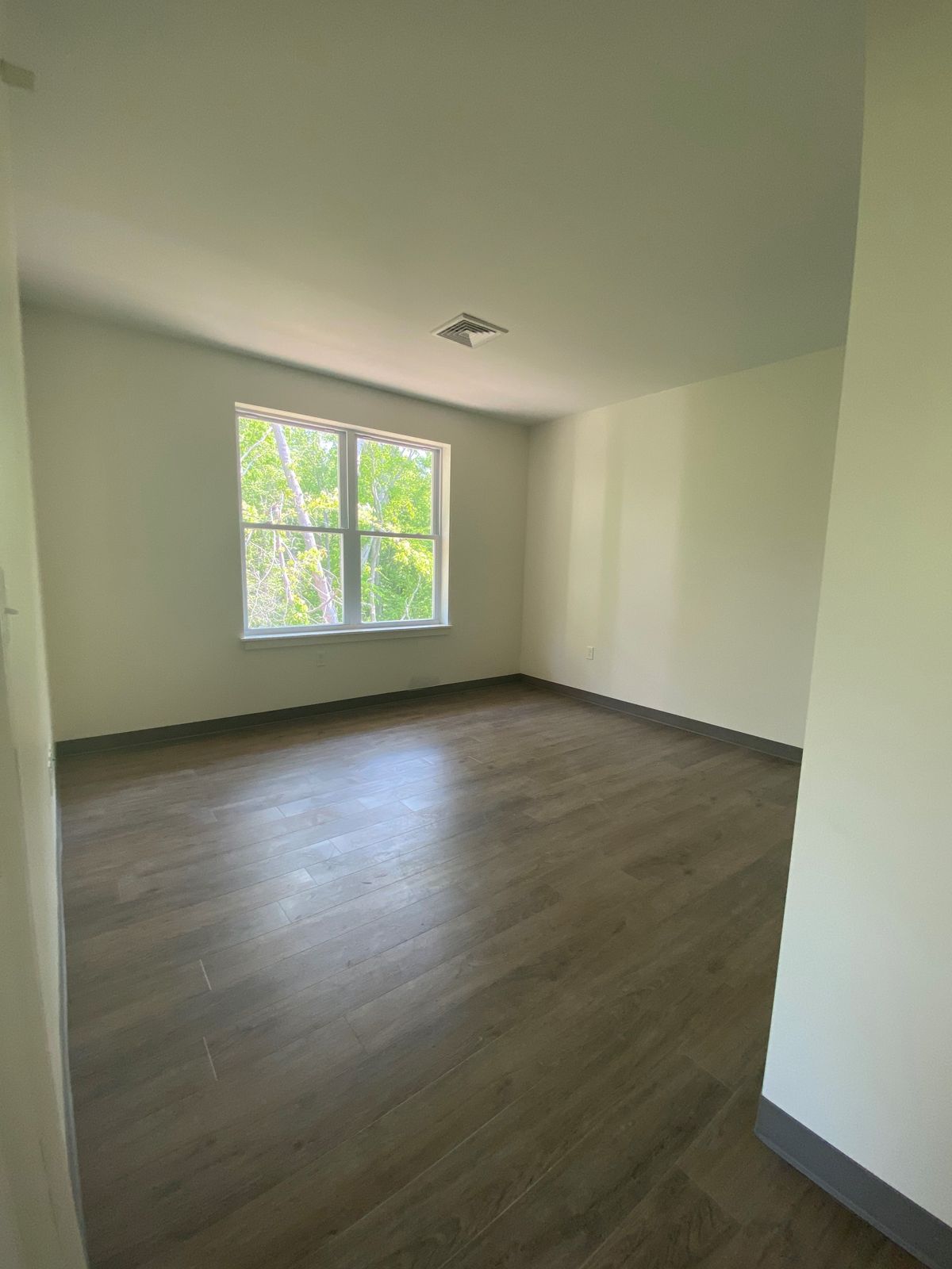 A bright, empty room with a large window and wooden flooring.