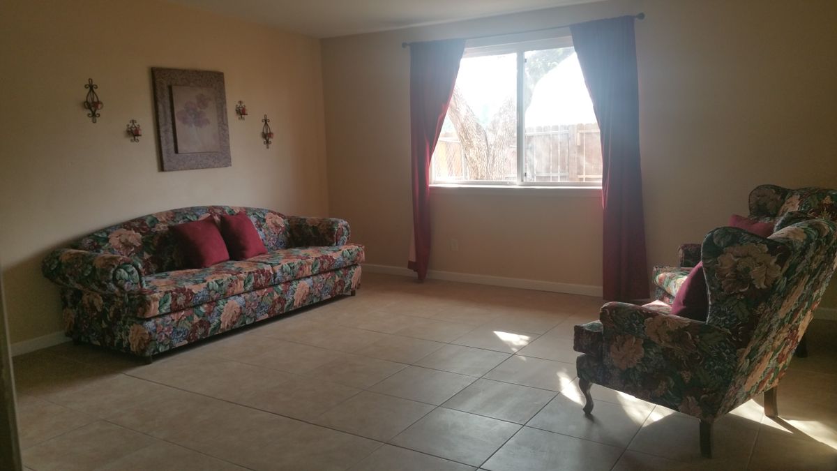 A cozy living room with a floral sofa and armchair, featuring a large window with curtains.