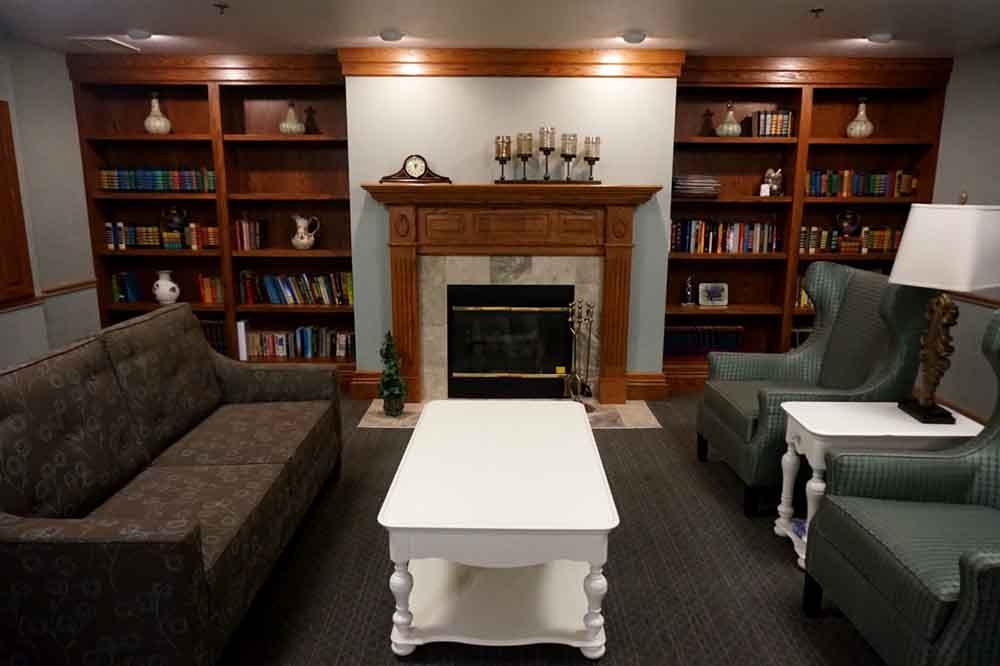 A cozy living room with a fireplace, surrounded by bookshelves and furnished with comfortable sofas and a white coffee table.