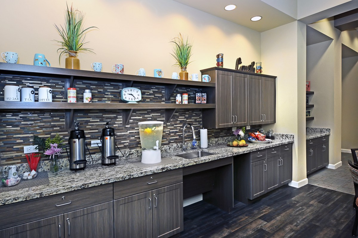 A modern kitchen area with granite countertops, cabinets, and a beverage station.