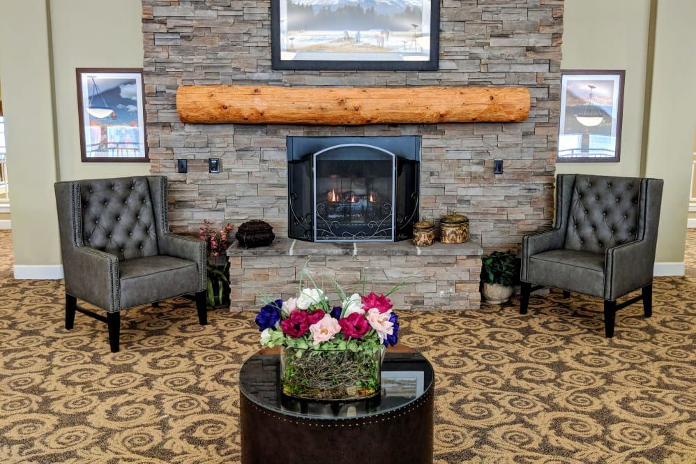 A cozy living room with a stone fireplace, decorated with armchairs and a coffee table featuring a colorful flower arrangement.